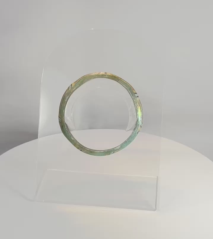 Rotating view of an ancient Roman mosaic glass bracelet with polychrome decoration, highlighting its multicolored striped pattern, archaeological iridescence, complete circular form, and craftsmanship from the Roman Imperial Period, circa 1st–4th century AD.