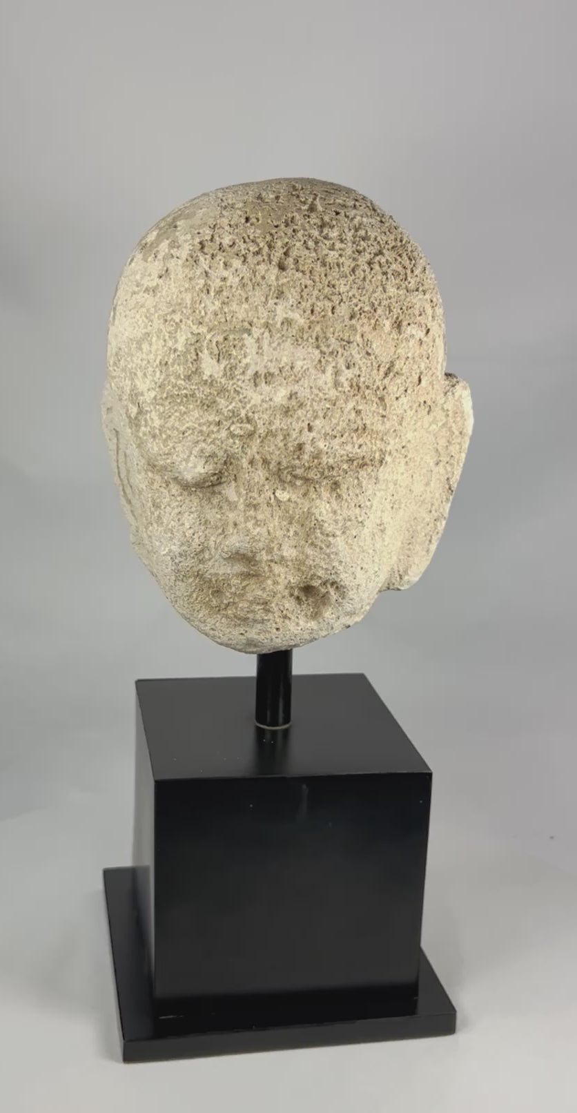Southeast Asian carved stone Buddha head with serene expression and closed eyes, 13th–14th century, mounted on a modern black stand, Burma or Thailand.