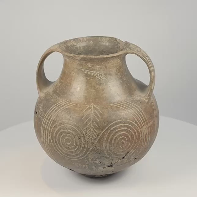 Rotating 360-degree video of an early Etruscan impasto spiral amphora, circa 700–650 BCE, showing its double handles, rounded body, incised spiral decoration, rim, base, and ancient surface patina.