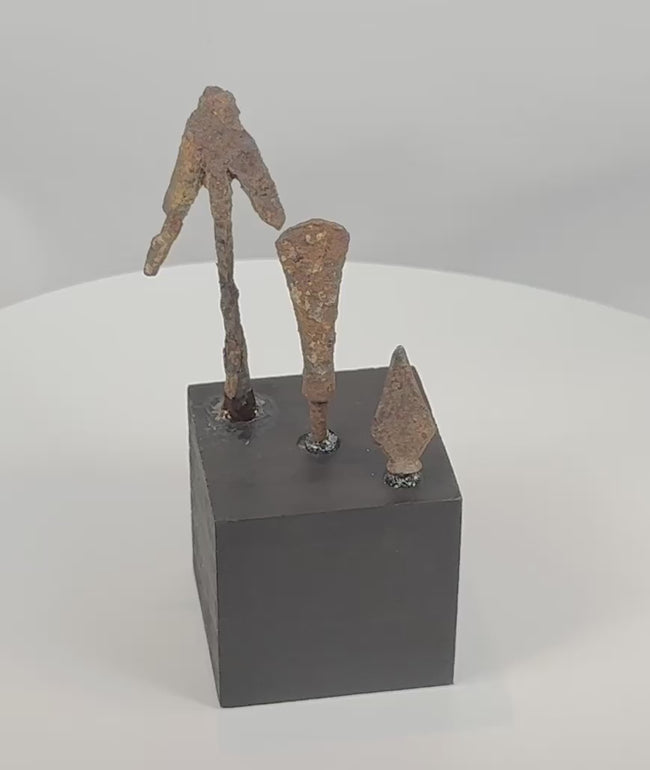 Rotating view of three Late Roman to medieval hand-forged iron projectile points, including a narrow lozenge-shaped arrowhead, a broader tanged bolt or javelin head, and a forked or barbed example, each mounted on a black display base