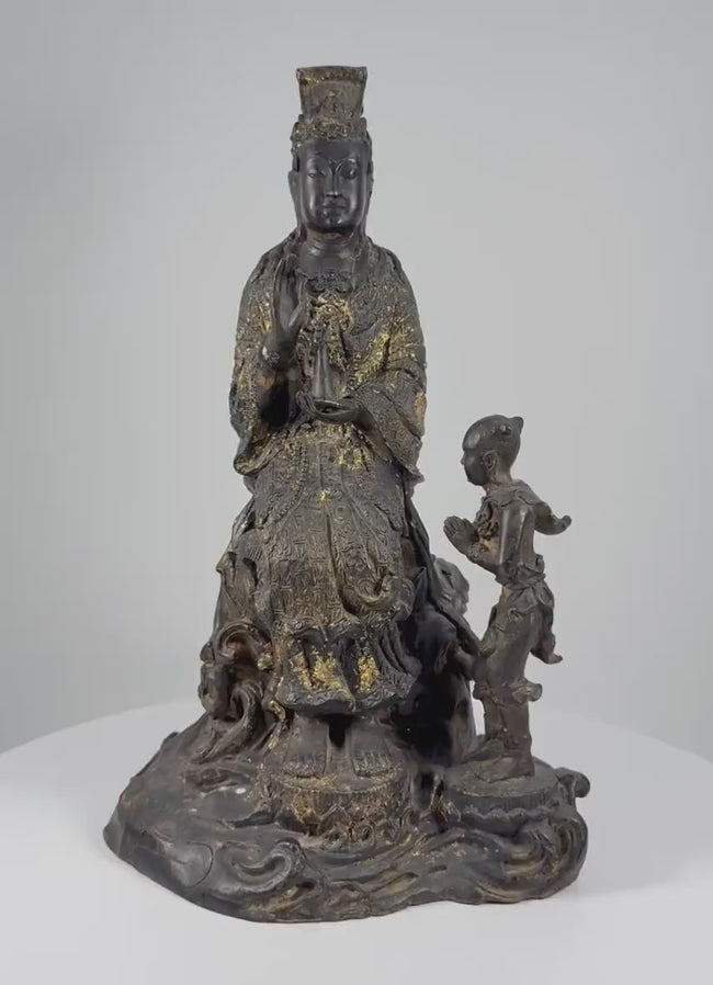 Video showcasing an antique Thai bronze Guanyin sculpture dating to circa 1900, highlighting the seated Bodhisattva of Compassion, child attendant, ornate lotus pedestal, intricate robes, traces of gold gilding, and naturally aged patina.