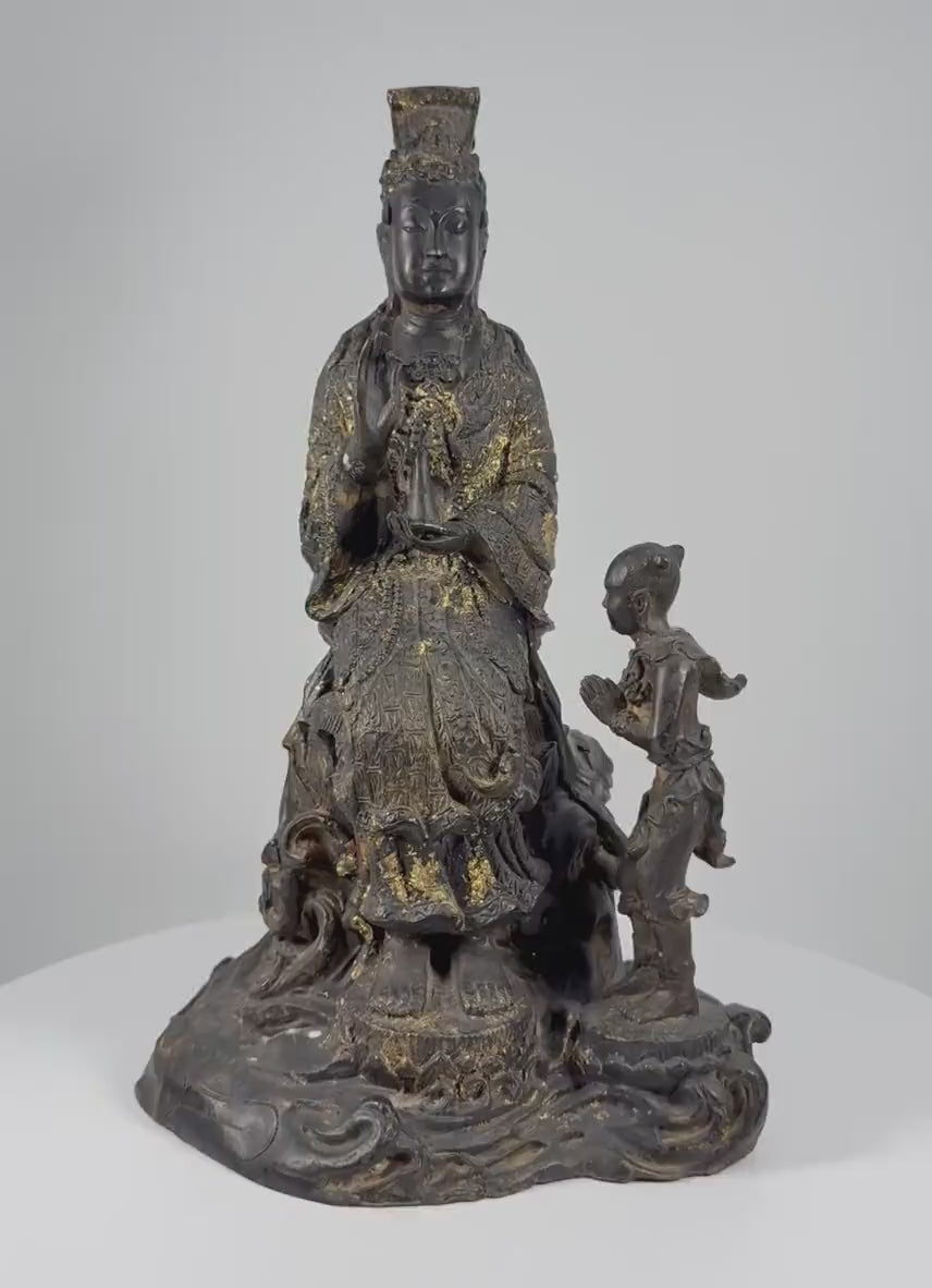 Video showcasing an antique Thai bronze Guanyin sculpture dating to circa 1900, highlighting the seated Bodhisattva of Compassion, child attendant, ornate lotus pedestal, intricate robes, traces of gold gilding, and naturally aged patina.