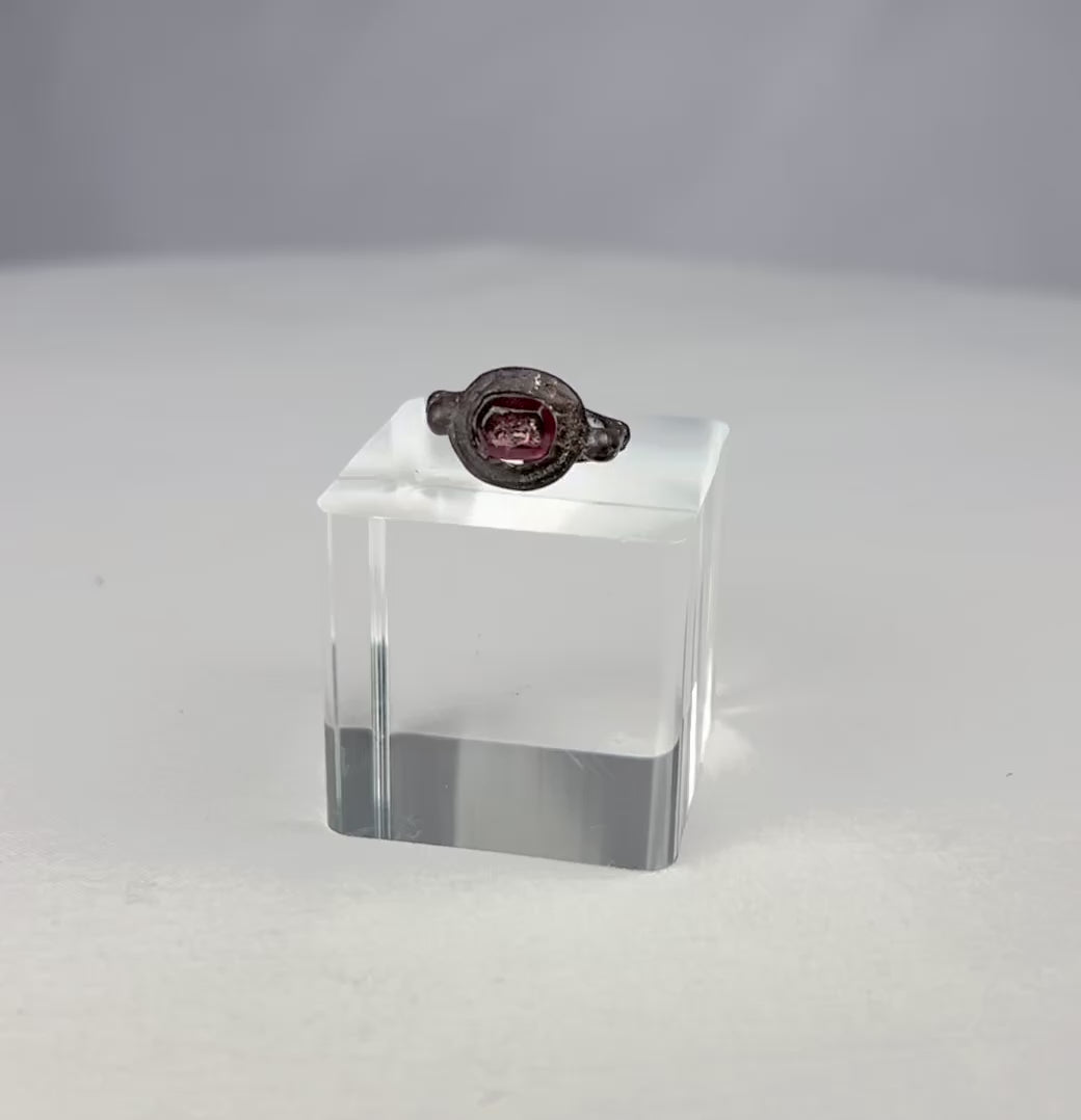 Ancient silver ring from the Eastern Mediterranean or Near East, Late Roman to Early Byzantine period (circa 300–600 CE), featuring a deep red garnet intaglio engraved with symbolic imagery, flanked by decorative silver nodes, preserving its historical elegance and craftsmanship.