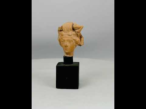 Ancient terracotta head fragment from the Greco-Roman world, circa 4th–1st Century BCE, showing naturalistic facial features and elaborate hairstyle, mounted on a modern black display base, Hellenistic and classical artistic style.