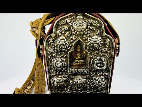 19th-century Tibetan portable shrine (gau) with silver repoussé Buddhist motifs and central glazed Buddha figure, set in embroidered red and gold fabric case with strap, photographed on a white background.