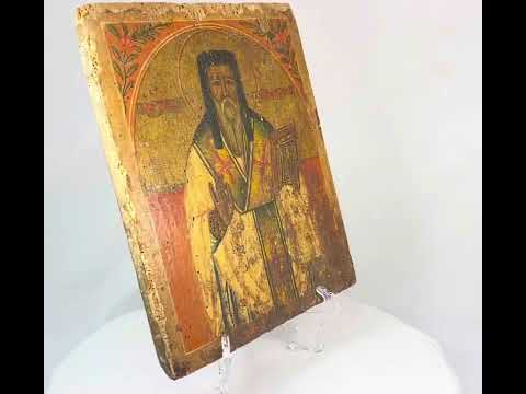 18th-century Russian religious icon panel showing a saint holding a Gospel book, hand-painted on wood with aged patina and craquelure, displayed on a stand.