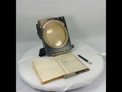 RAF WWII navigational computer with rotating aluminum dial, Bakelite adjustments, original fabric straps, pencil, and open flight notebook showing handwritten navigator’s notes.