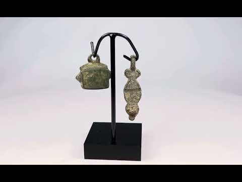 Ancient Roman bronze artifacts, circa 1st–4th century CE, including a patinated pendant and small ritual bell displayed on a custom stand.