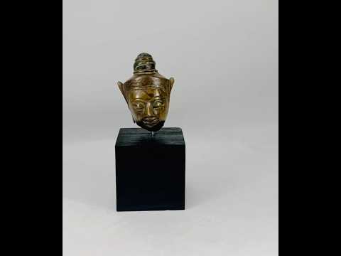 Bronze Buddha head on black display base, featuring serene facial expression, pointed ushnisha, and natural greenish patina, likely from Thailand or Cambodia, 18th–19th century CE.