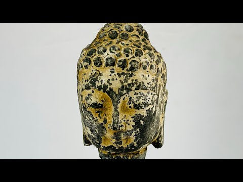 Antique carved stone Buddha head from Southeast Asia, likely Thailand or Cambodia, 18th–19th Century. Features serene meditative expression, curled hair, and traces of original pigments. Mounted on a marble base, reflecting Buddhist artistry, spiritual symbolism, and historical craftsmanship of the region.