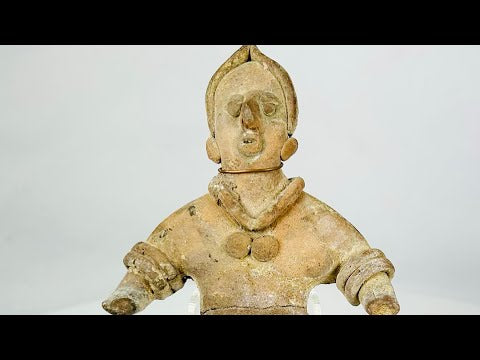 Ancient Pre-Columbian terracotta figurine, circa 300–900 CE, depicting a stylized human figure with detailed jewelry and headdress, shown standing with arms extended.