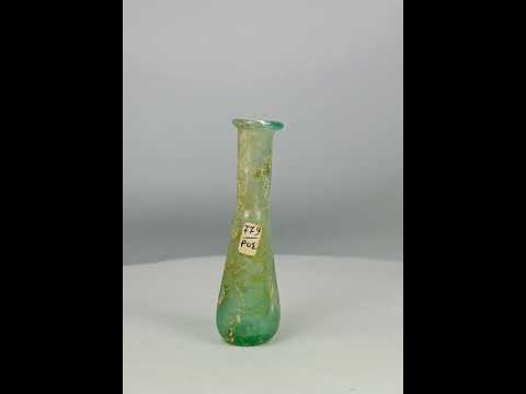 Ancient Roman hand-blown glass bottle, 1st Century BCE–4th Century CE. Elongated cylindrical neck with rounded conical body, out-sprayed folded rim, and delicate translucency. Includes original archaeological tag. Used for ointments, perfumes, or medicines, reflecting Roman glassmaking innovation, daily life, and luxury trade.
