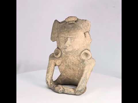 Ancient Mesoamerican terracotta figurine depicting a seated human with helmet-like headpiece, large circular ear ornaments, and hollow cavity in back for ritual use, Classic Period (200–800 AD).