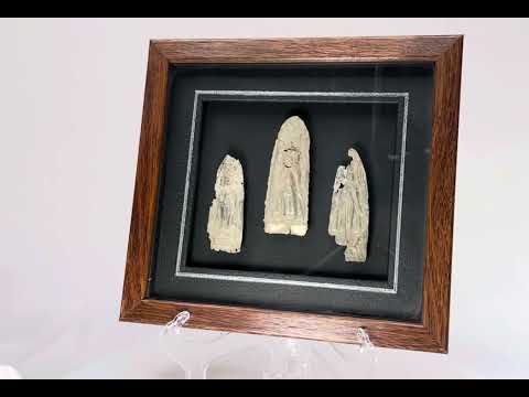 Framed set of three antique cast metal votive plaques from Cambodia or Thailand, 16th–17th Century CE. Central plaque depicts a seated Buddha in meditation, flanked by attendant or deity figures, with intricate engraved details. Mounted on a custom wooden frame, showcasing devotional artistry and Theravāda Buddhist iconography.