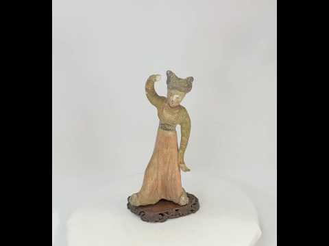 Tang Dynasty low-fired terracotta figurine of a female dancer, mid-performance pose with raised arm, twin-knot chignon hairstyle, traces of original red-orange and black mineral pigments on robe and facial features, mounted on a wooden display base, 11 inches tall, circa 618–907 CE.