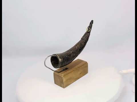 360 degree video of a Tibetan bronze ritual powder horn with engraved decorative motifs, curved shape, mounted on a wooden display stand, 19th century.