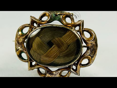 Antique Victorian mourning brooch with braided human hair under beveled glass, set in an ornate gold-plated brass Gothic Revival frame, circa 1850–1880.