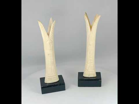 Pair of carved Egyptian ivory sistrum handles on black display bases, featuring stylized figures and decorative motifs, dating to the Third Intermediate Period, circa 1070–664 BCE.