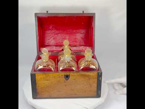 Georgian-era wooden tantalus box with red-painted interior, containing four gilded glass decanters with stoppers, used for securely storing and displaying spirits, early 19th century.