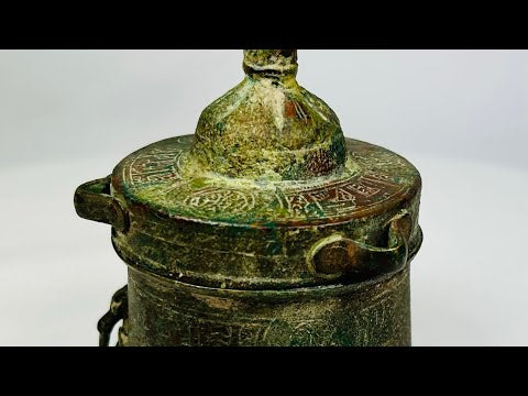 Antique Islamic Khorassan bronze inkwell, cylindrical form with domed lid, engraved with intricate geometric and vegetal motifs, rich green patina from centuries of age, dating to the 10th–12th century, historically used by Islamic scholars and scribes as part of manuscript tradition.
