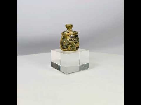 Ancient Roman or Parthian glass cosmetic jar, circa 2nd–3rd century CE, with rounded body, fitted lid topped by a knob finial, and luminous iridescent patina developed over centuries.
