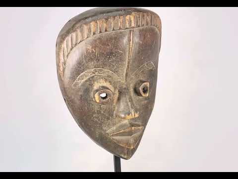 Antique Baule tribal mask from Ivory Coast, early 20th century, hand-carved wood with natural patina, oval face, almond-shaped eyes, and stylized features displayed on a stand.