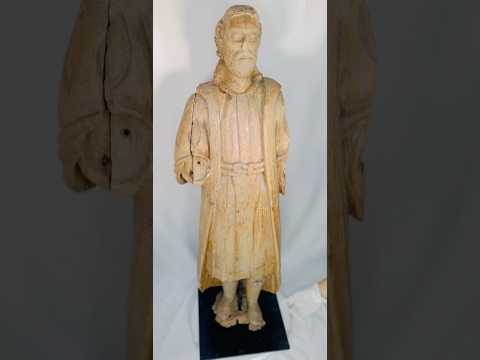 Antique Spanish Colonial wooden Santo statue depicting a standing saint with detailed robes and facial features, mounted on a black display base, 18th–19th century.