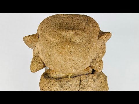 Ancient Pre-Columbian terracotta figurine with stylized facial features and unique headdress, likely Mayan or Zapotec, circa 500–1500 CE.