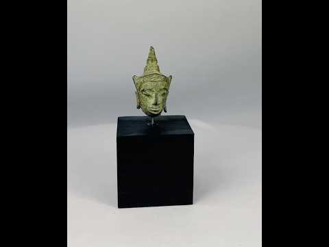 Small antique Southeast Asian bronze Buddha head, likely from Thailand or Cambodia, 16th–17th Century CE. Features serene expression, elongated earlobes, pointed ushnisha, and natural green patina. Originally part of a larger statue, serving as a devotional object reflecting Buddhist spiritual symbolism, artistry, and enlightenment.