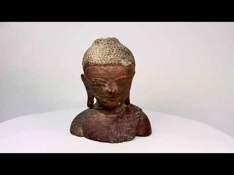 19th-century Southeast Asian wooden Buddha bust, likely Thailand or Burma, with serene features, red lacquer, gold gilt remnants, and metal chain detail.