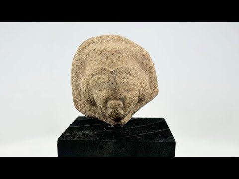 Fragmentary terracotta head with stylized arched brows, almond-shaped eyes, defined beard and mustache, and detailed coiffure; likely part of a votive or ritual figure from the Near East/Eastern Mediterranean, circa 1st millennium BCE; mounted on a custom black display base.