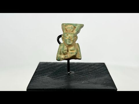 Miniature pale blue-green faience amulet of lion-headed goddess Sekhmet, front-facing with tripartite wig and crown traces; suspension hole on reverse; mounted on black wood stand; Egypt, Third Intermediate Period, circa 1070–664 BCE.
