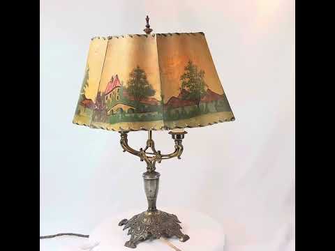 Antique Art Nouveau table lamp, circa 1920s, with ornate cast metal base and original hand-painted parchment shade depicting cottages, windmills, and trees, a decorative European lighting piece with warm pastoral charm.