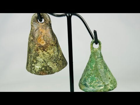 Pair of Ancient Roman cast bronze bells, 1st–4th century CE, conical form with suspension loops, green patina, and mounted display stand.