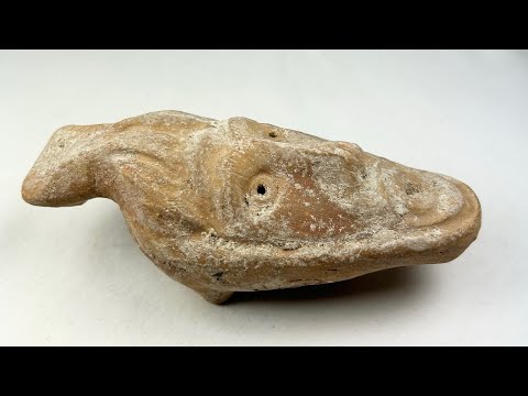 Ancient Byzantine terracotta oil lamp featuring a molded human face with open mouth spout, dating from the 5th to 7th century AD, showing aged surface encrustations.