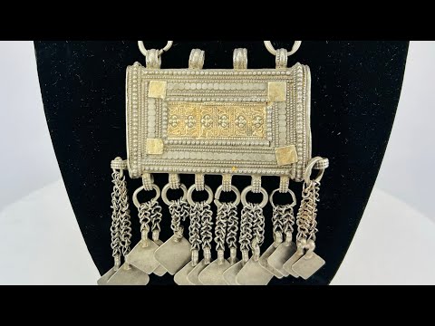 19th-century Omani silver hirz necklace with central rectangular Koran holder, intricate filigree and gilded accents, suspended from a multi-strand chain with decorative dangles.