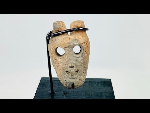 Miniature anthropomorphic mask pendant carved from bone, featuring hollowed eyes, prominent nose ridge, open mouth, and twin suspension holes; mounted on custom display stand; Western Mexico, Colima/Nayarit region, circa 300 BCE–300 CE.
