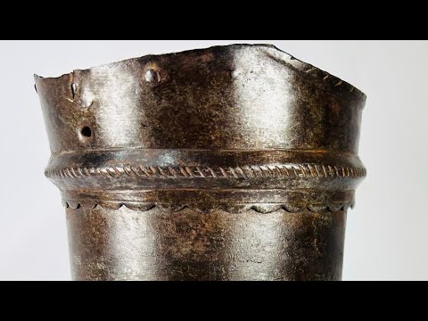 16th-century European upper arm armor, cannon-style plate with scalloped edge detailing, aged patina, and mounted on a display stand.