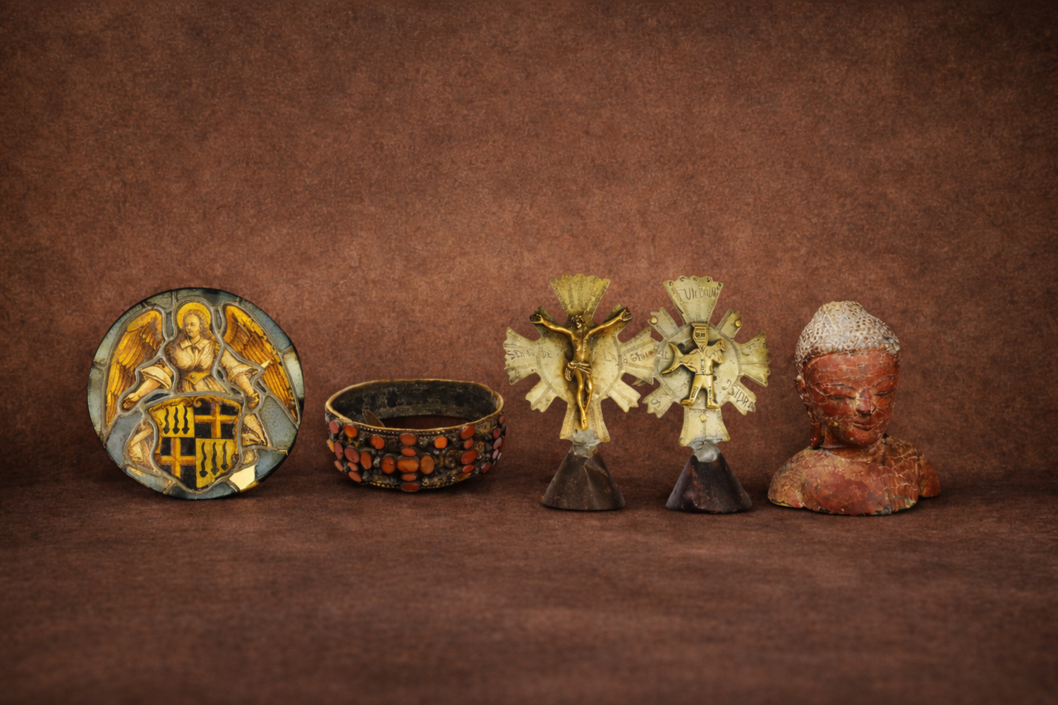Curated collection of rare historical artifacts including a 16th-century stained glass angel medallion, Russian bridal belt, Spanish Colonial brass crucifixes, and Southeast Asian Buddha bust displayed against a warm textured backdrop.