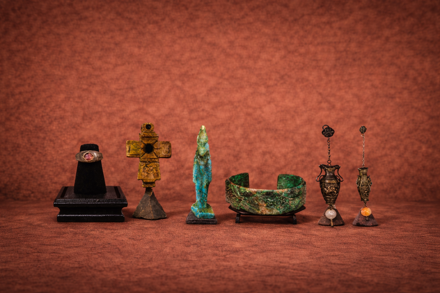 Curated collection of ancient artifacts including gemstone ring, medieval cross, turquoise figurine, patinated bronze cuff, and ornate antique earrings displayed on warm brown background.