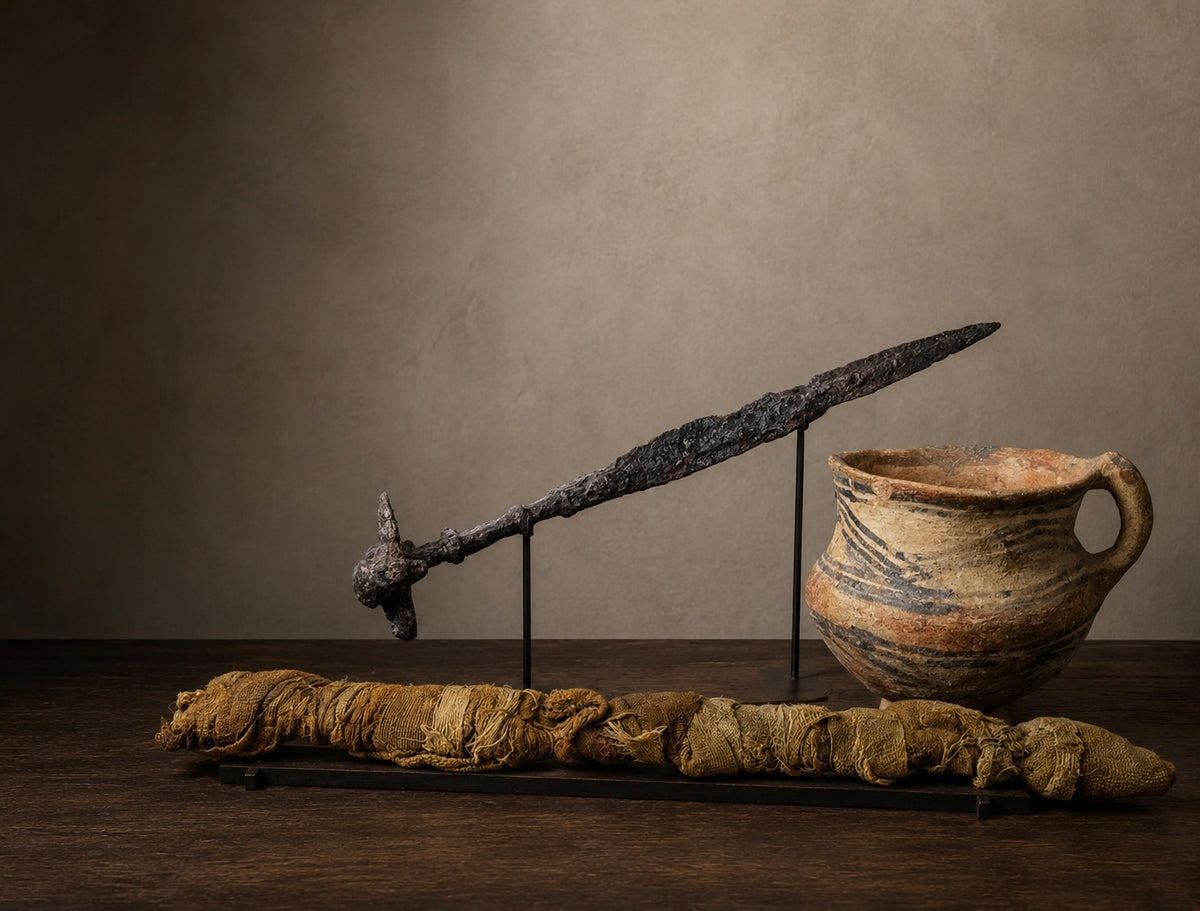 Egyptian crocodile mummy, Iron Age Luristan sword and Neolithic Chinese painted pottery vessel displayed in a museum-style setting.